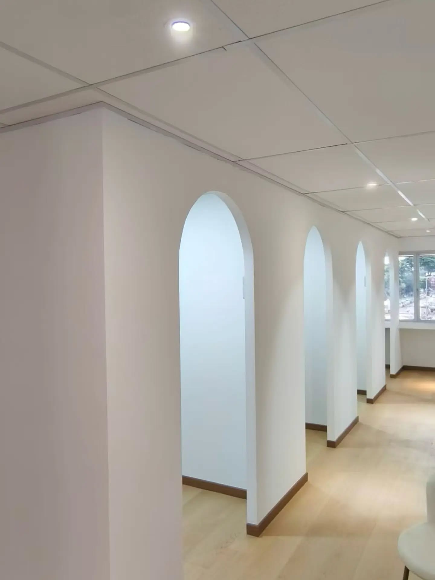石膏板隔墙围成的办公室走廊，拱形门洞，木纹地板，嵌入式筒灯。