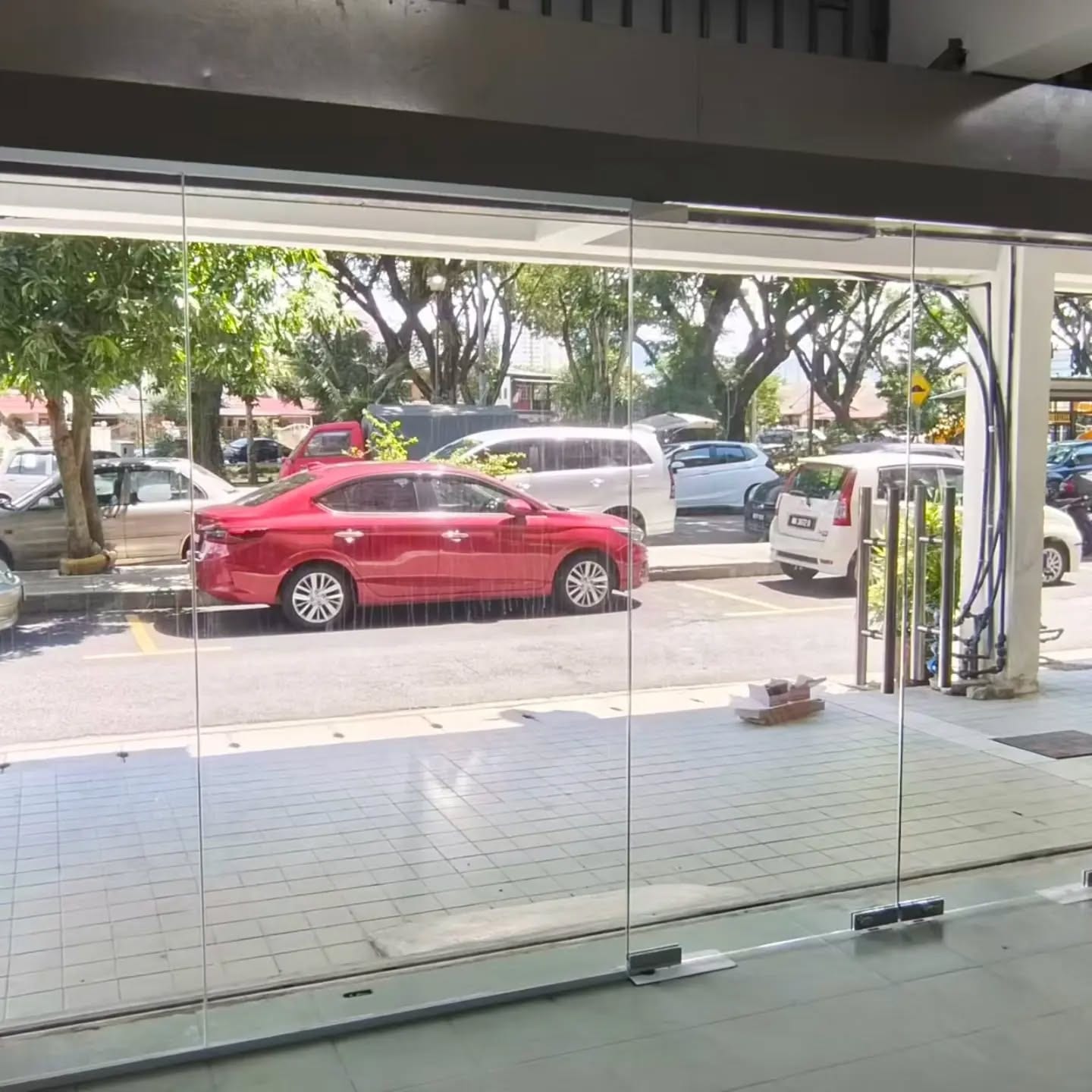 从店内看出去的无框玻璃店门，门外是街道和停着的车。